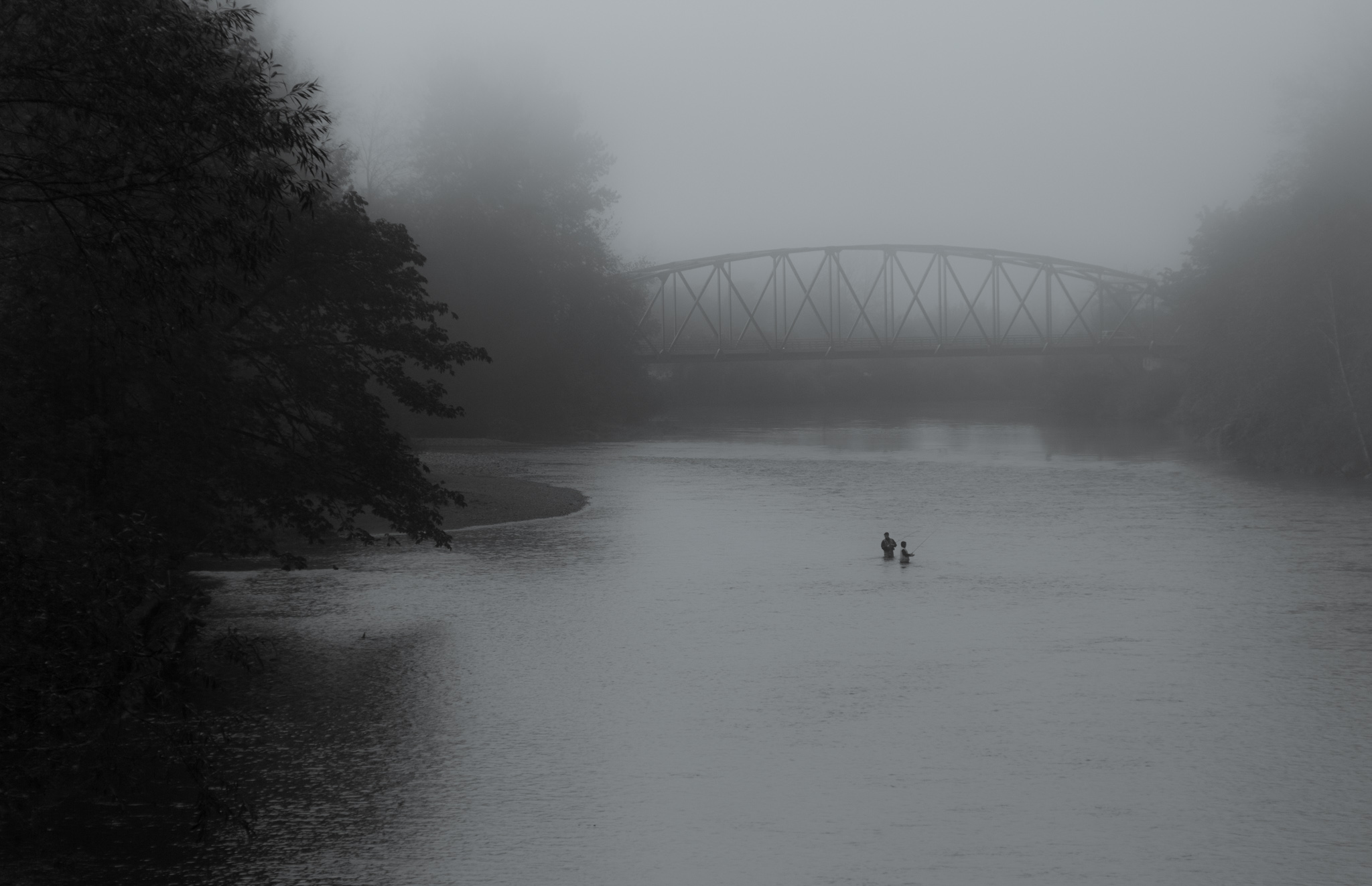 A misty river scene with a bridge and two fisherman in the distance.
